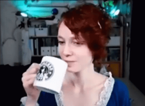 a woman with blue hair and red sweater sipping from a white mug