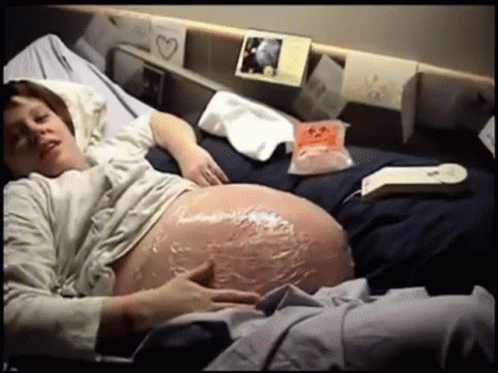 a pregnant person laying down in a bed with some paper