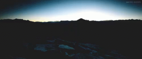 the sun peeking behind a mountain in the dark