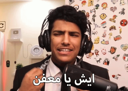 man in suit and tie with headphones holding microphone with arabic writing on wall behind him