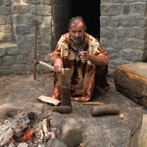 man sitting in a cave holding a hammer next to a fire place