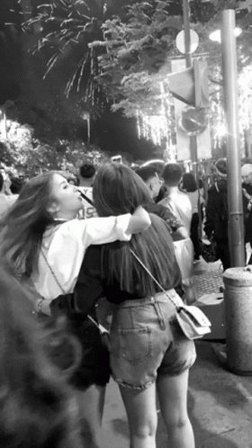 two people hug near a crowd with fireworks in the background