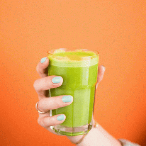 a woman is holding up a green drink