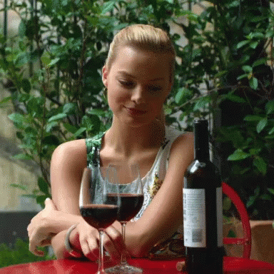 a lady sitting with a glass of wine and an empty bottle