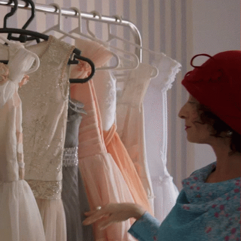 woman wearing blue cap looks at dresses hanging from racks