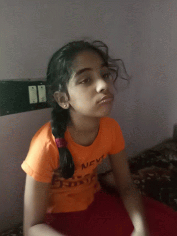 a little girl in a blue shirt sitting on the bed