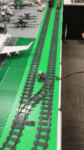 a green train track sits on the floor next to a train station