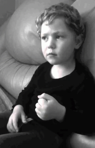 a child with the head resting on his arms sits on a couch