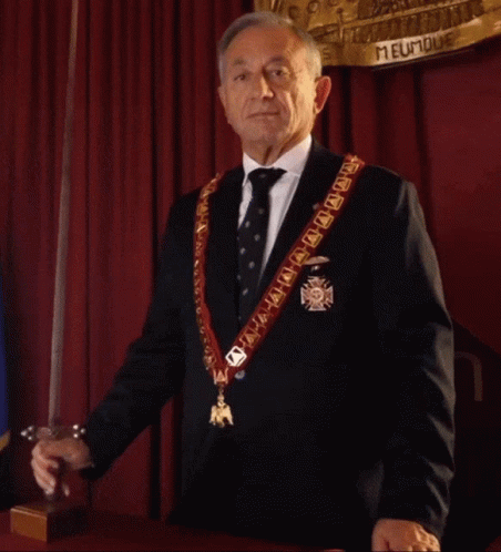 a man holding a sword and wearing an order of fame sash
