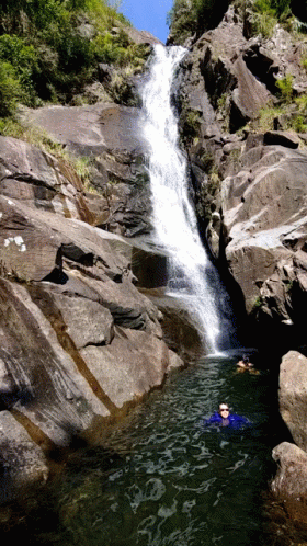 a group of people in the water below a waterfall