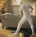 a white man wearing all white is walking towards a couch in a blue room
