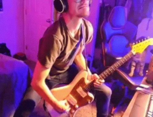 a man in grey shirt playing a guitar and headphones