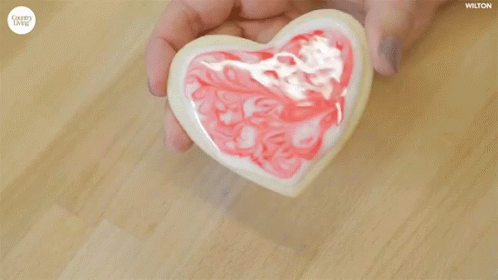 hands hold a heart shaped glass bowl while sitting on top of the table