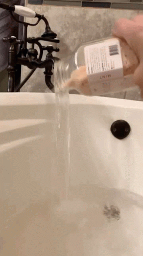 a hand in glove pours water into a bathtub
