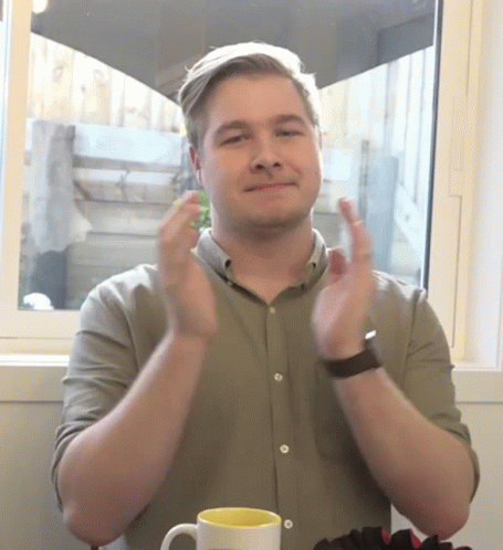 a man with his hands up over his face and two mugs on the table in front of him