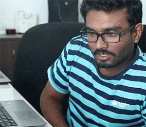 a man wearing a striped shirt and glasses is typing on his laptop