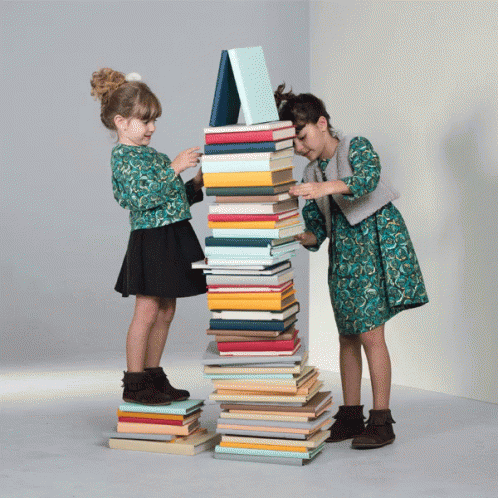 there are two girls that are standing near piles of books
