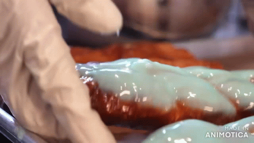 the people in white gloves are putting sauce on some doughnuts