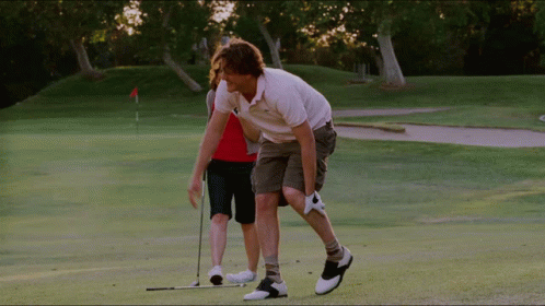 two people stand on a golf course with one putting the ball