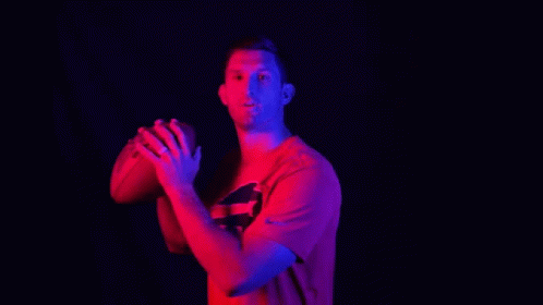a young man wearing a tshirt throwing a basketball in the dark