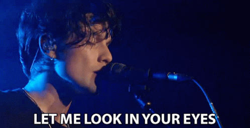a person on stage in front of a microphone with text that reads let me look in your eyes