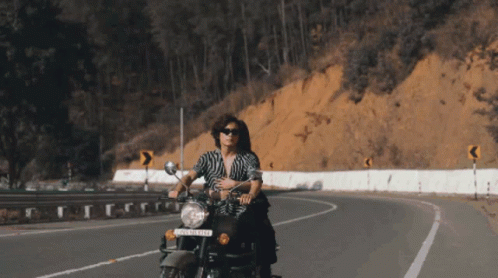 a woman rides a motorcycle down a winding road