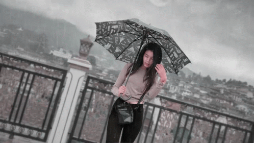 a woman stands beneath an umbrella in the rain