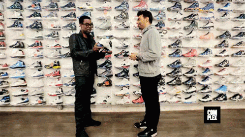 two men stand by an enormous wall full of shoes