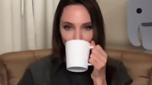 a woman sitting in a chair holding a cup in front of her mouth