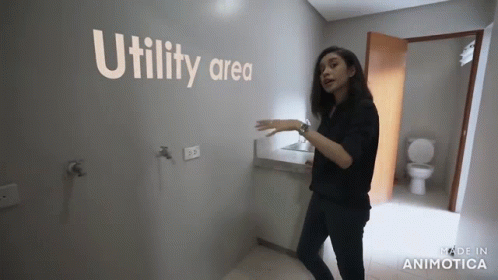 a woman walking past a bathroom wall with a toilet