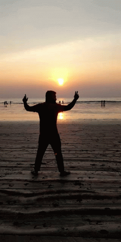 silhouette man standing on beach with arms outstretched with people in background