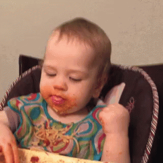 a toddler playing with food in his high chair