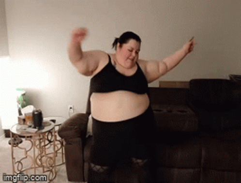 a fat woman standing in front of a couch and holding soing up