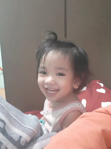 a baby girl smiling while sitting on a bed