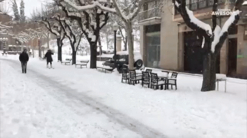 people walk along a snowy sidewalk in the daytime