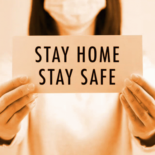 a woman holding up a sign that says stay home stay safe