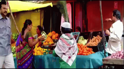 a man dressed in indian attire standing next to a fruit stand