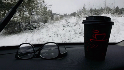 coffee cup sitting on dashboard near glasses next to trees