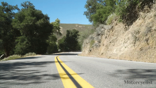 a motorcycle driving on a road next to a hill