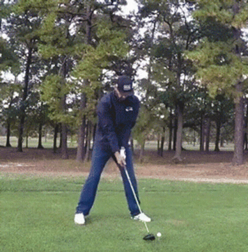 a man swings a golf club in an open green area