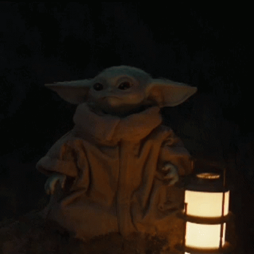 an adult baby yoda sitting on top of a table next to a light bulb