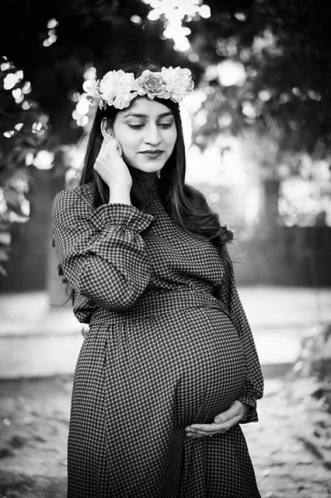 a pregnant woman poses in front of a tree with flowers on it's head