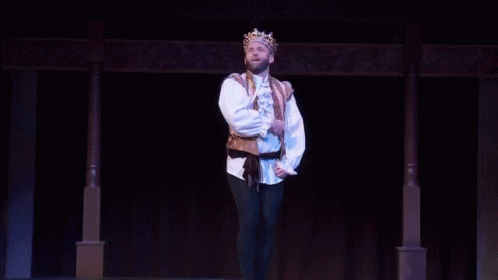 a male in a white shirt and a crown standing on a stage