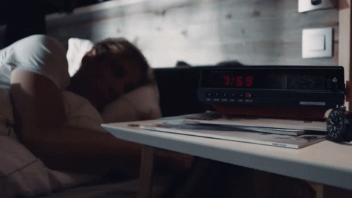 someone sleeps on a bed beside an alarm clock
