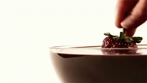 someone touching a single strawberry that is on top of a glass
