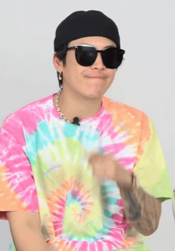 a young man wearing sunglasses sitting down with a tie dye shirt on