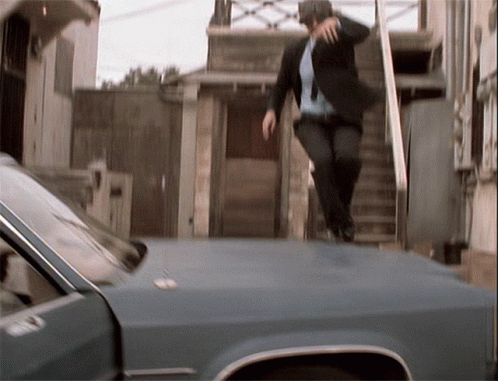 a man in suit jumping from the side of a car