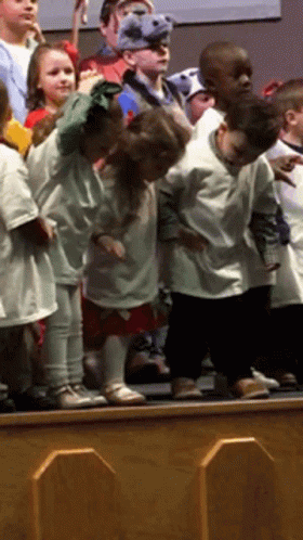 a line of children in white clothing standing on top of a blue stage