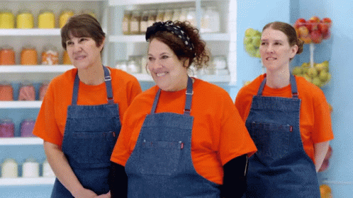 three women wearing brown aprons standing in front of shelf with blue containers
