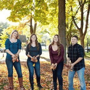 four people posing in front of a bunch of leaves